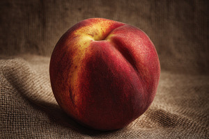 One peach on natural jute background, a Photo by Virgo Studio