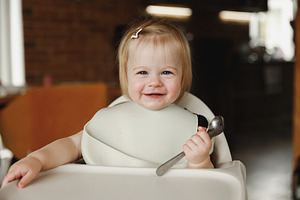 Infant girl or toddler sitting on high chair. Eating food by herself using spoo, a Person Photo by Lenor4ik