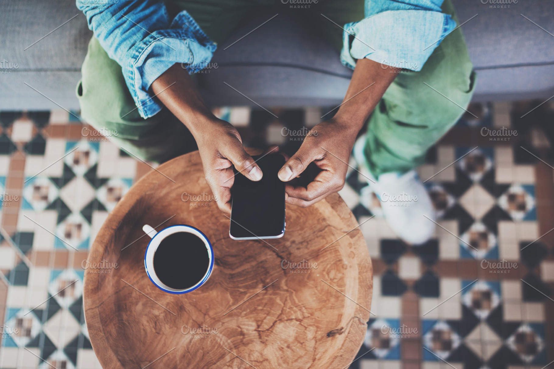 Top view of african man using smartphone while sitting on sofa at home.Concept people working with mobile gadget.Black coffee wooden table.Blurred background., a Business Photo by SFCRCH MOCKUPS