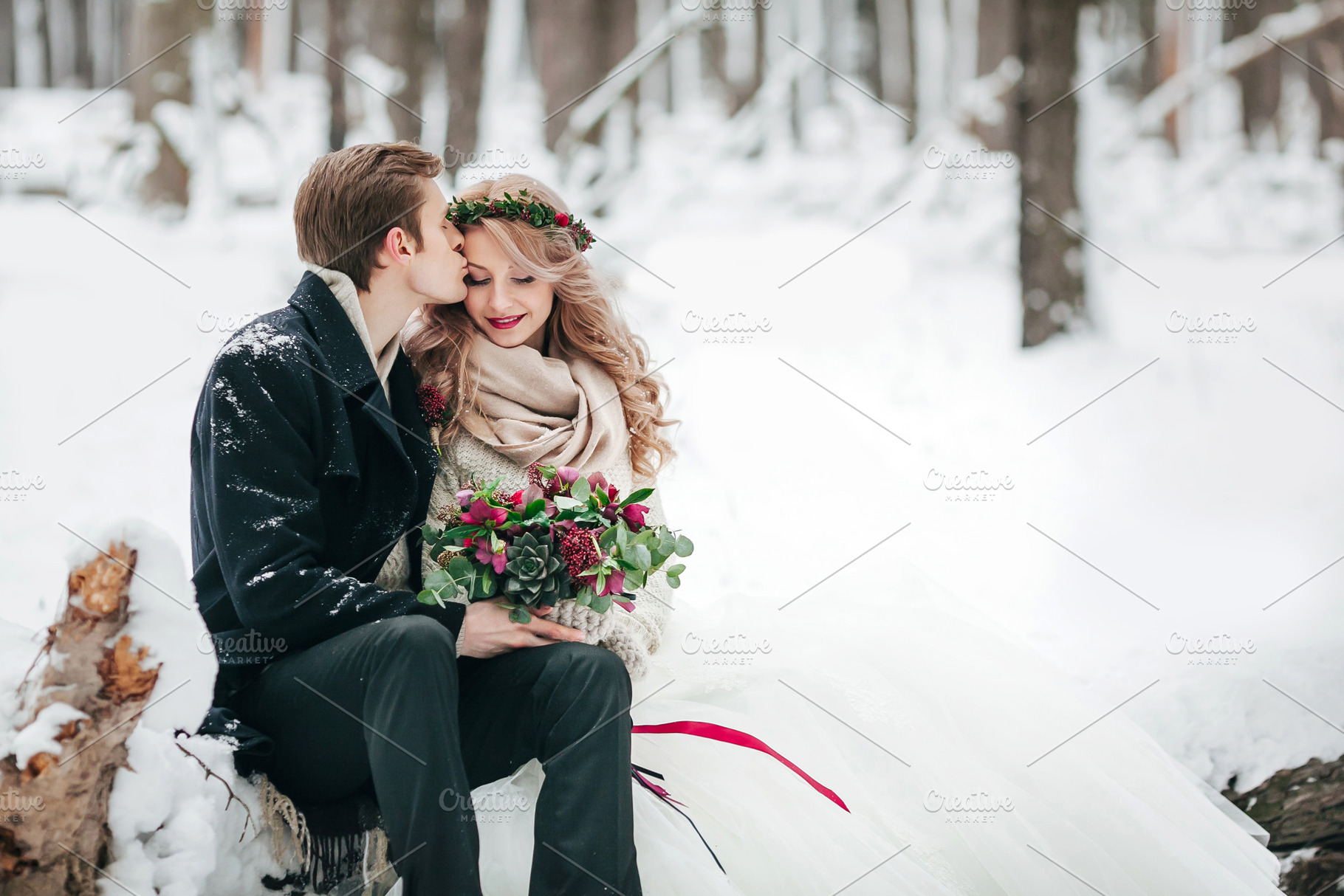 Groom is kissing his bride on the temple on background of the snowy forest. Winter wedding. Artwork, a Food & Drink Photo by Stahov