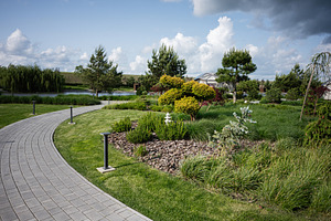 Beautiful landscaped park with pathway and greenery under a partly cloudy sky, a Photo by AS photostudio