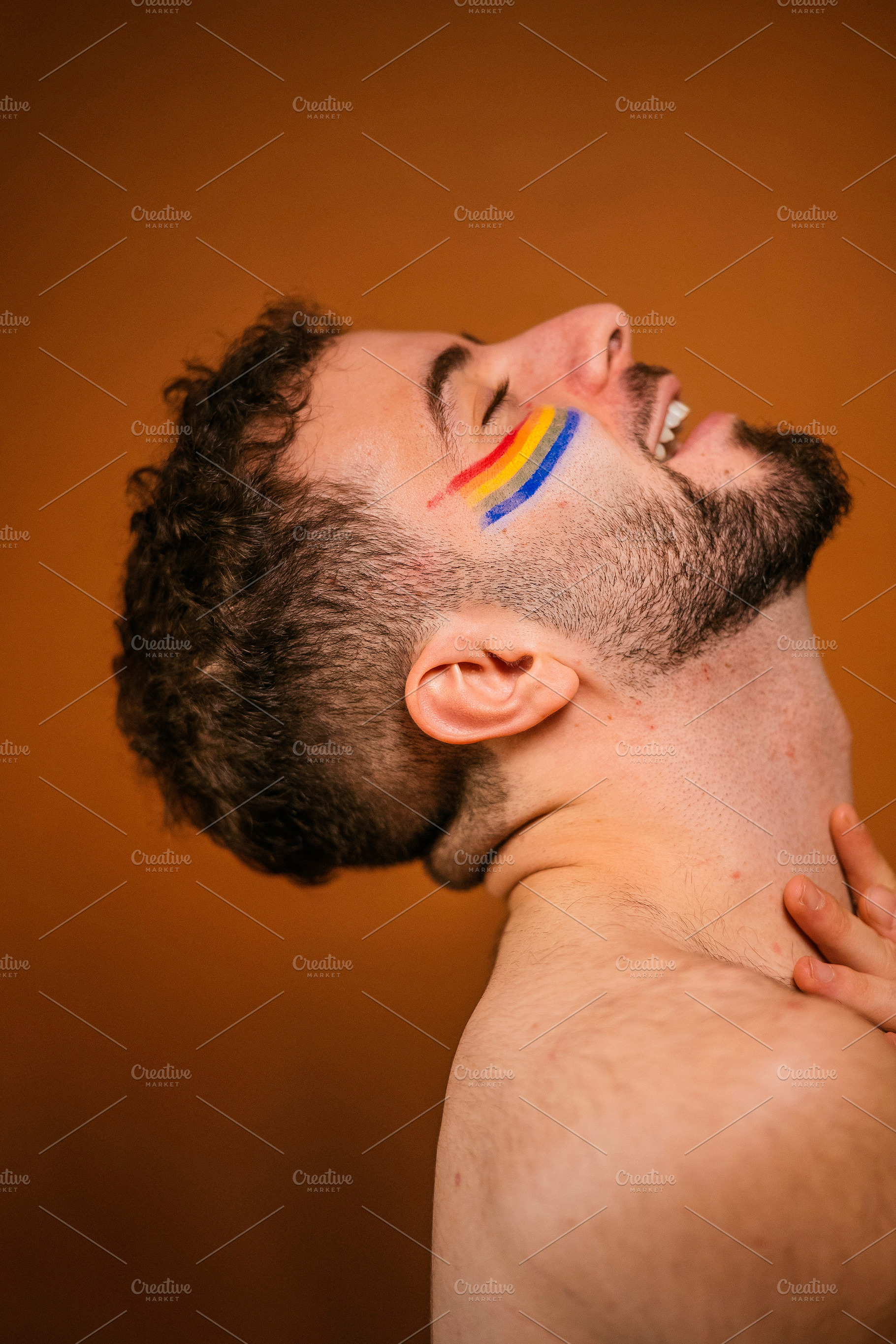 Bearded man expressing pride with rainbow face paint, a Photo by karrastock