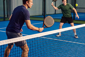 Men playing dynamic padel match on blue court with glass walls i