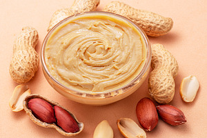 Bowl of peanut butter and peanuts around it on beige background., a Food & Drink Photo by Volff