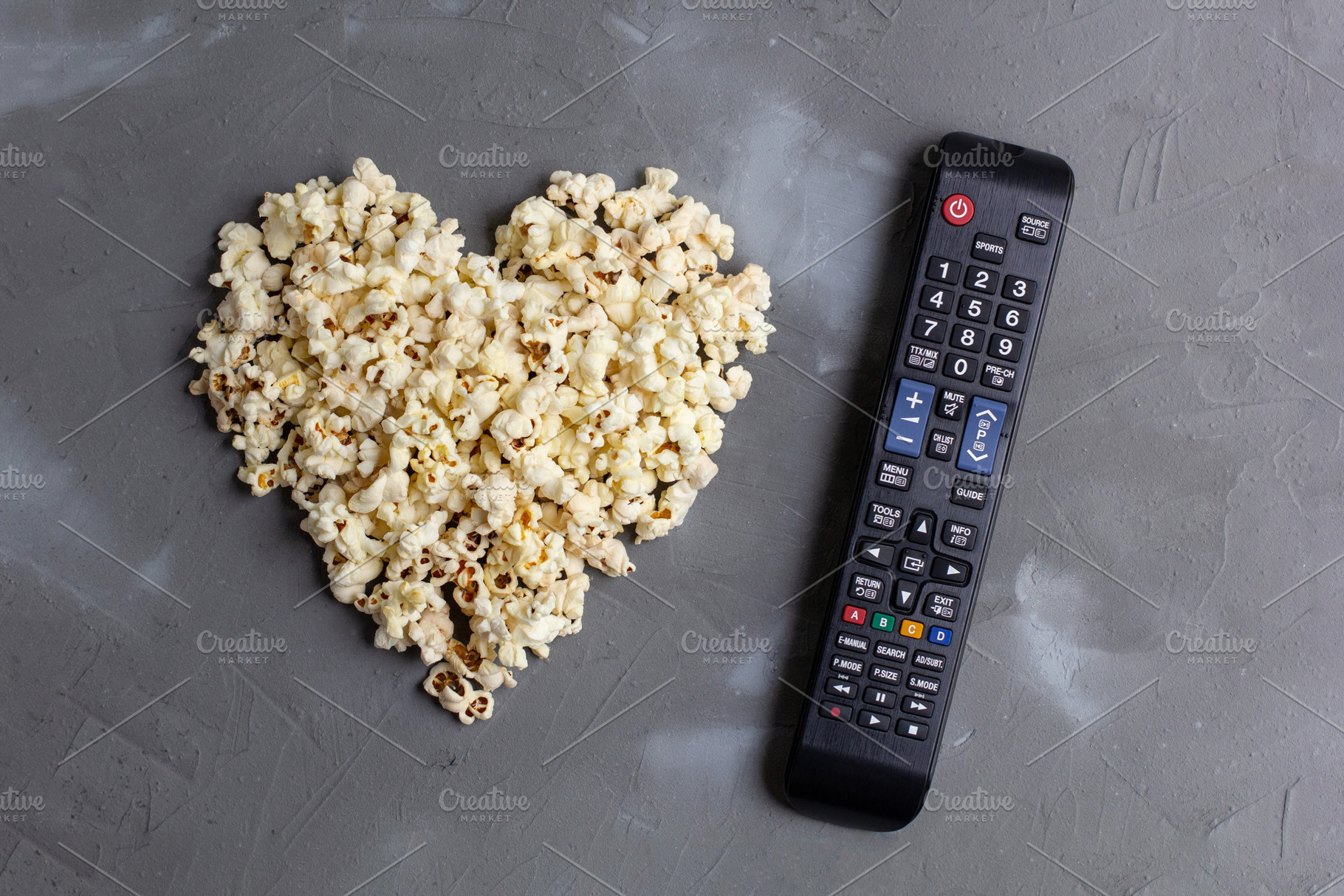 Popcorn in the shape of a heart and TV remote on grey stone background, a Food & Drink Photo by dashtik