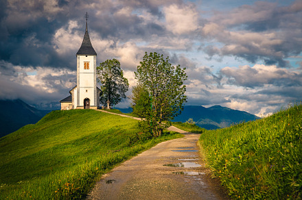 Dirty road and Saint Primoz church, an Architecture Photo by Alpine Dreams