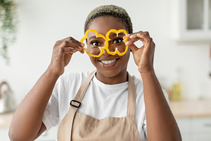 Happy millennial african american lady housewife in apron have fun and puts pie, a Person Photo by Prostock-Studio