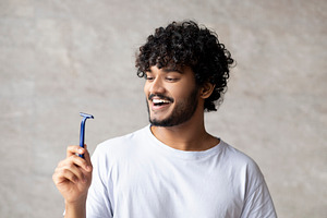 Body care concept. Happy indian man holding razor and smiling, standing in bath, a Person Photo by Prostock-Studio
