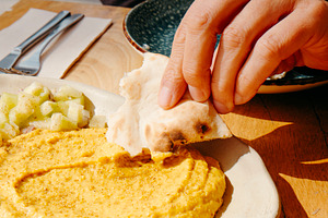man dips a piece of naan bread on hummus, a Photo by Nito