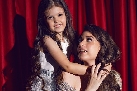 beautiful young woman in a shiny dress is sitting with a daughter child on red, a Person Photo by SaulichPhoto