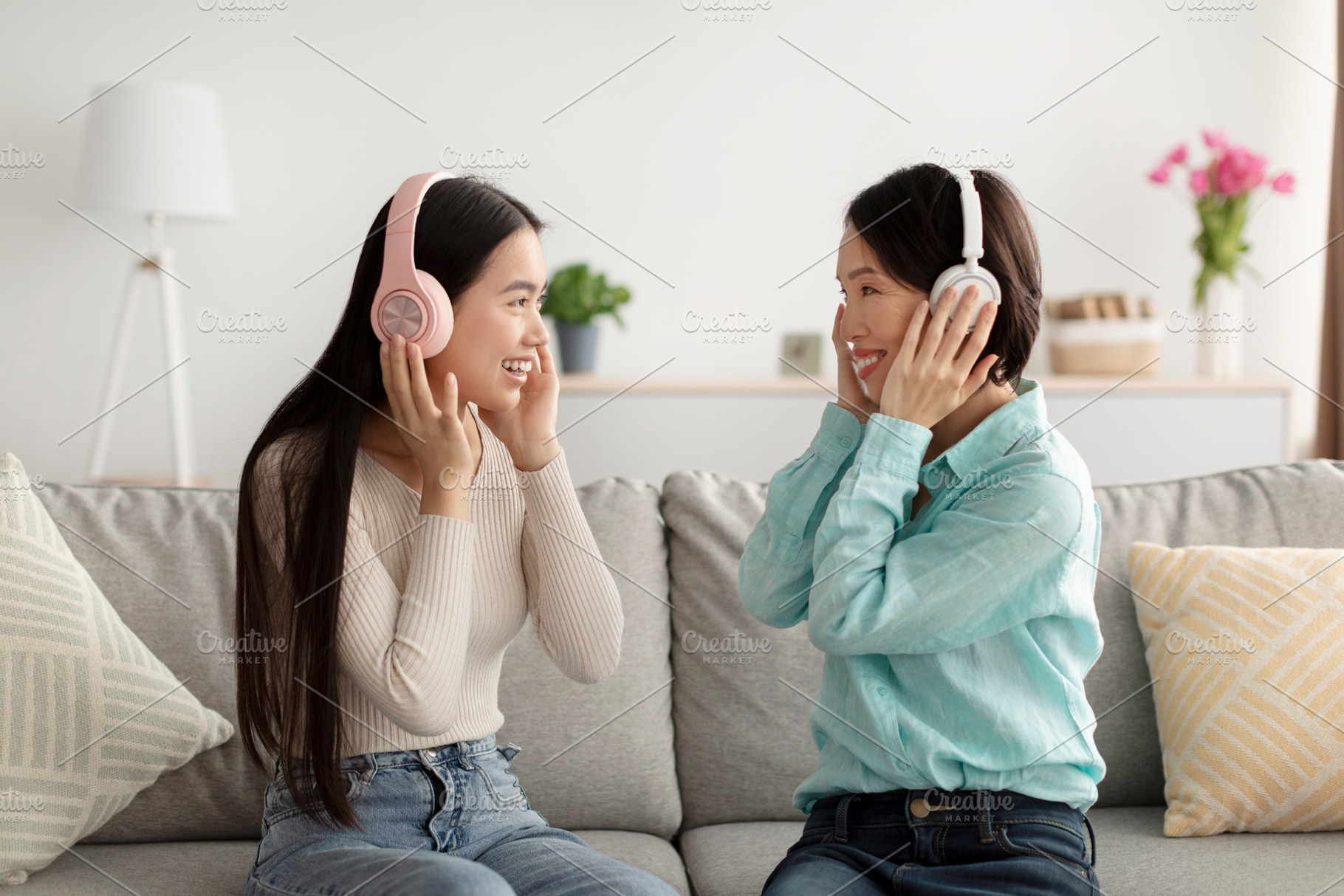 Happy young Asian woman and her mature mother in headphones listening to music, a Photo by Prostock-Studio