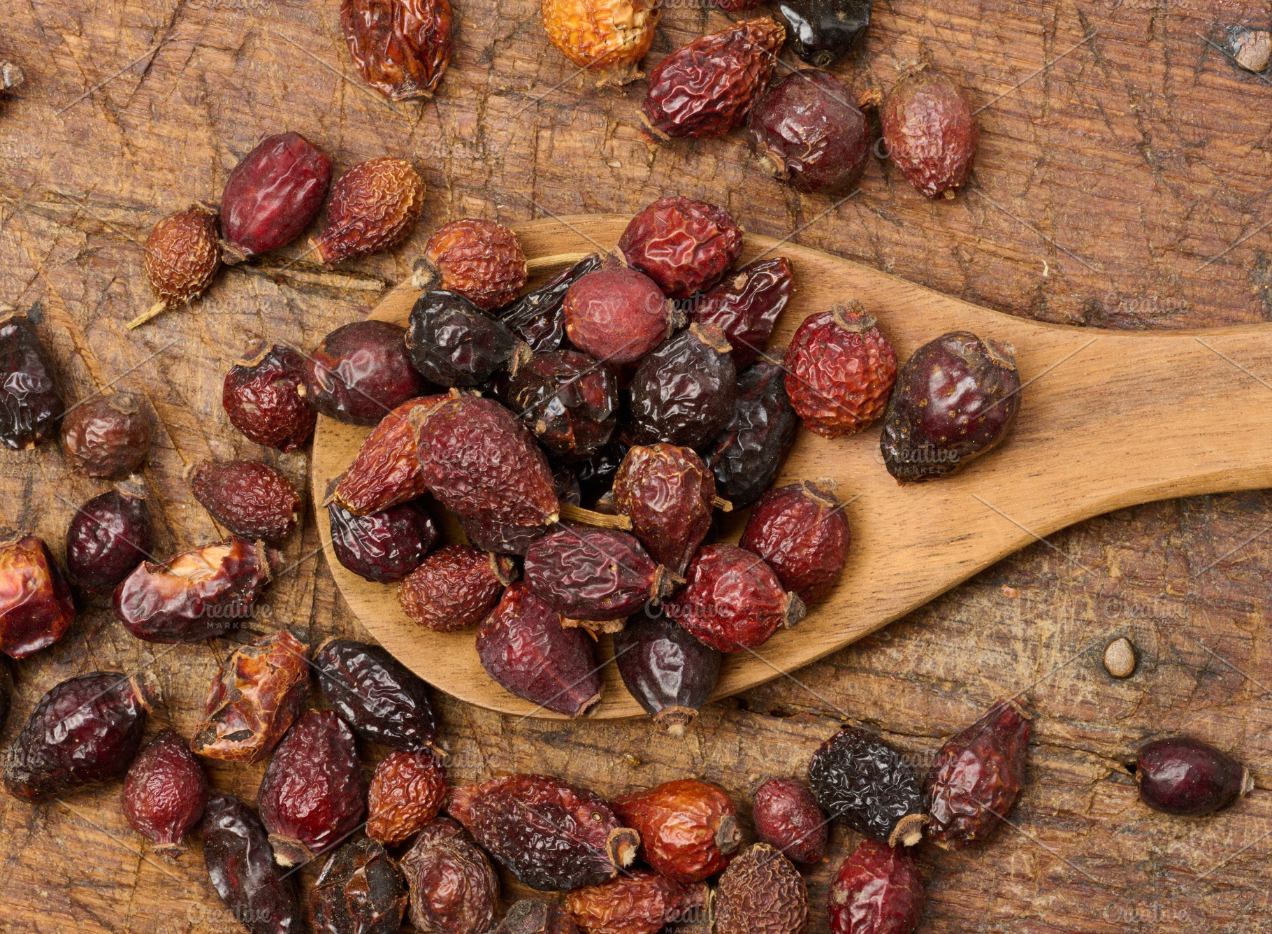 Dried rosehip fruits in a wooden spoon and on a table close-up., a Food & Drink Photo by ndanko