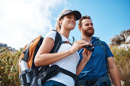 Hiking, binoculars and love with a couple on a mountain, enjoying a view while walking out in nature together. Summer, adventure and backpack with a man and woman sightseeing outdoor in the mountains, a Photo by Peopleimages.com