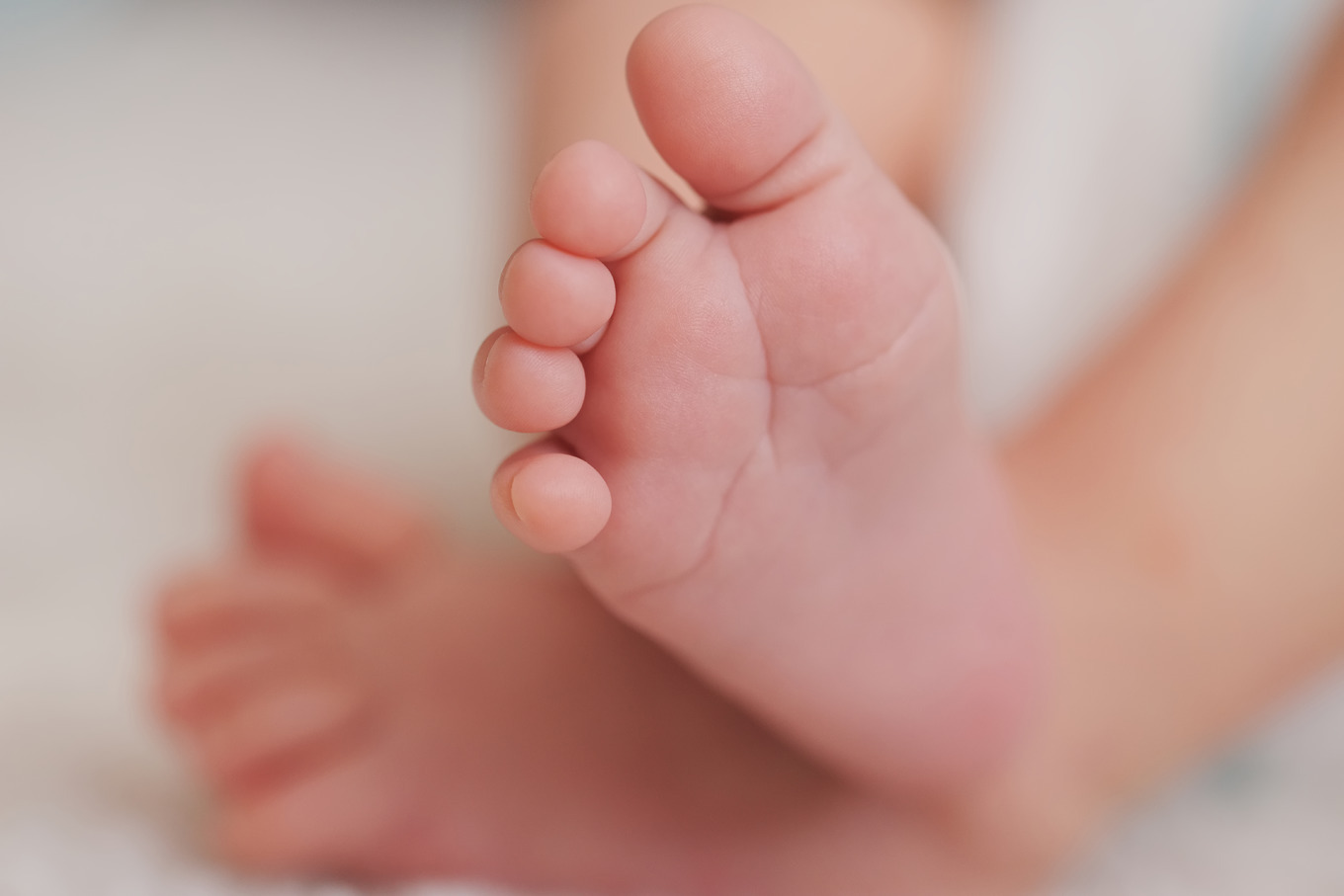 Mother holds little foot of newborn baby containing baby, feet, and