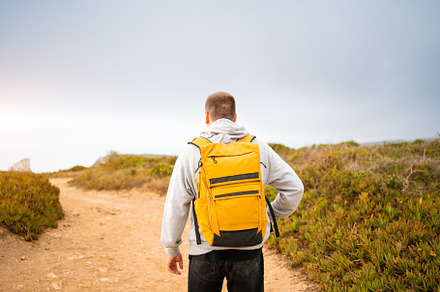 Rear-view young man traveler with yellow backpack, a Photo by andreonegin market