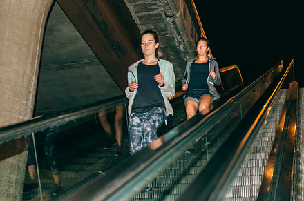 Women friends training running down escalator in city at night