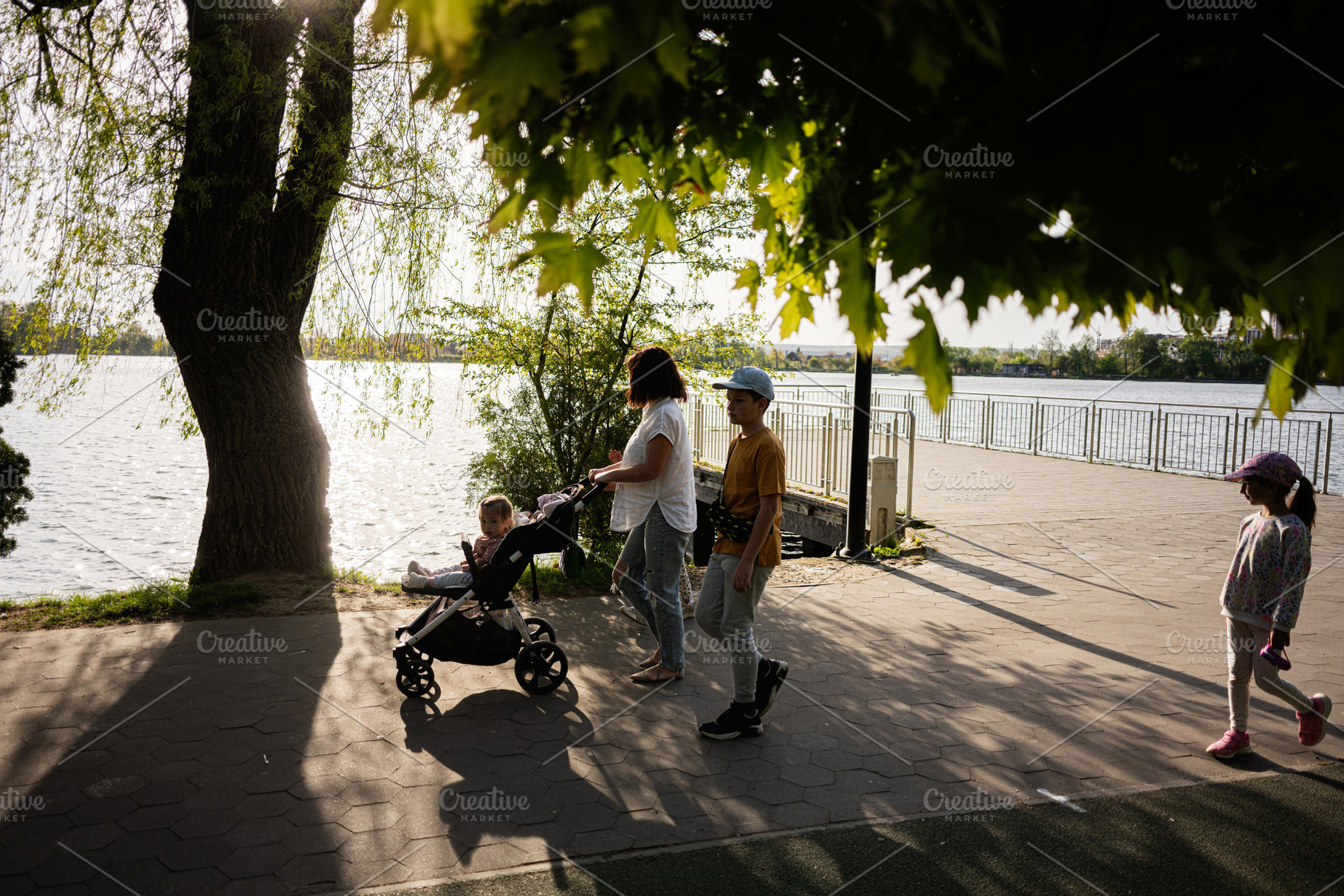 Family walking along a scenic river promenade during a sunny day, a Person Photo by AS photostudio