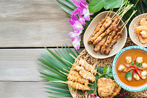 Satay skewers and shrimp with rice, sauces, and orchids arranged, a Photo by Dvoevnore photos