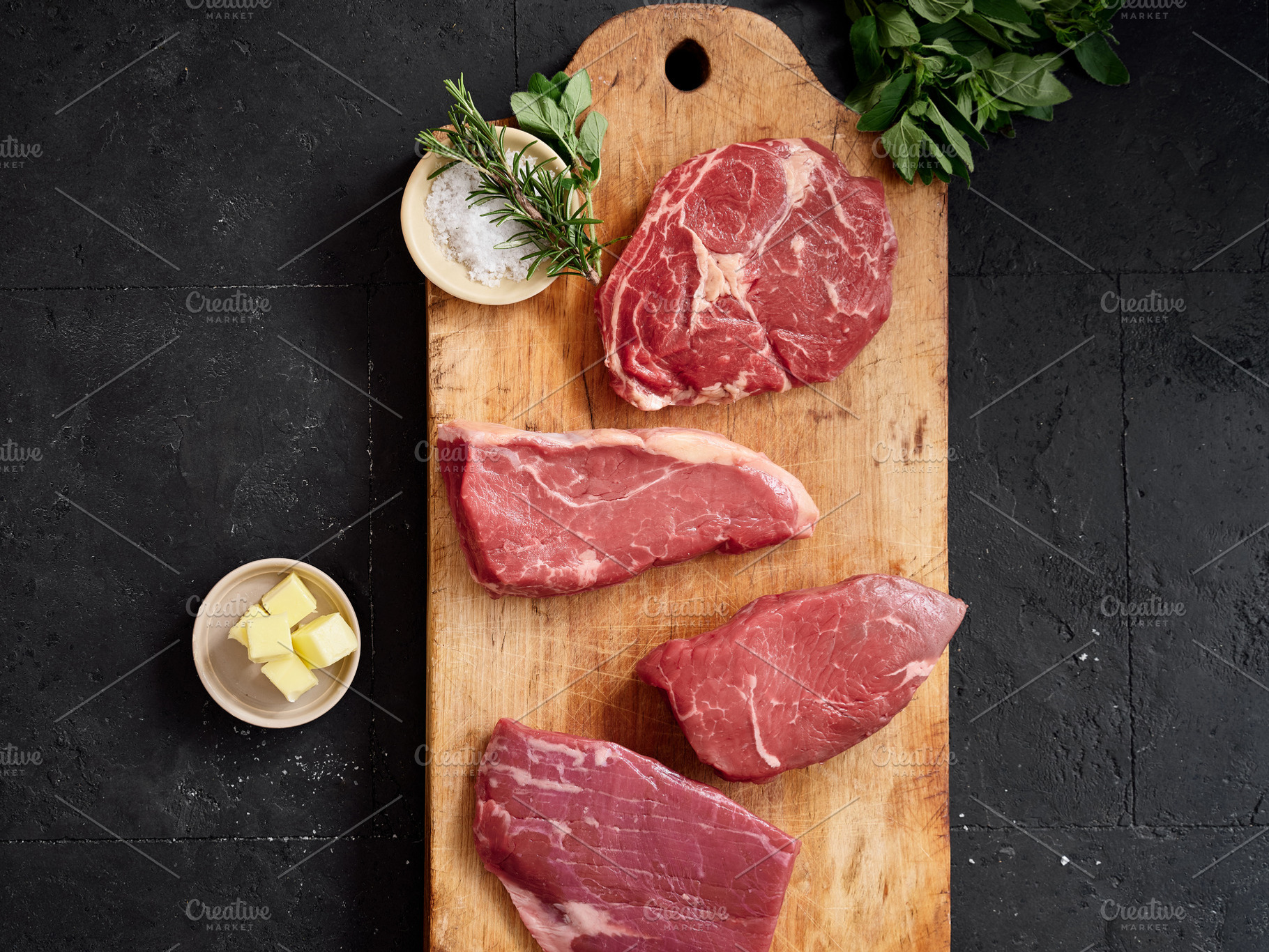 Raw rib-eye, roast beef, flank and rump steak on a wooden cutting board with he, a Food & Drink Photo by Asya Nurullina