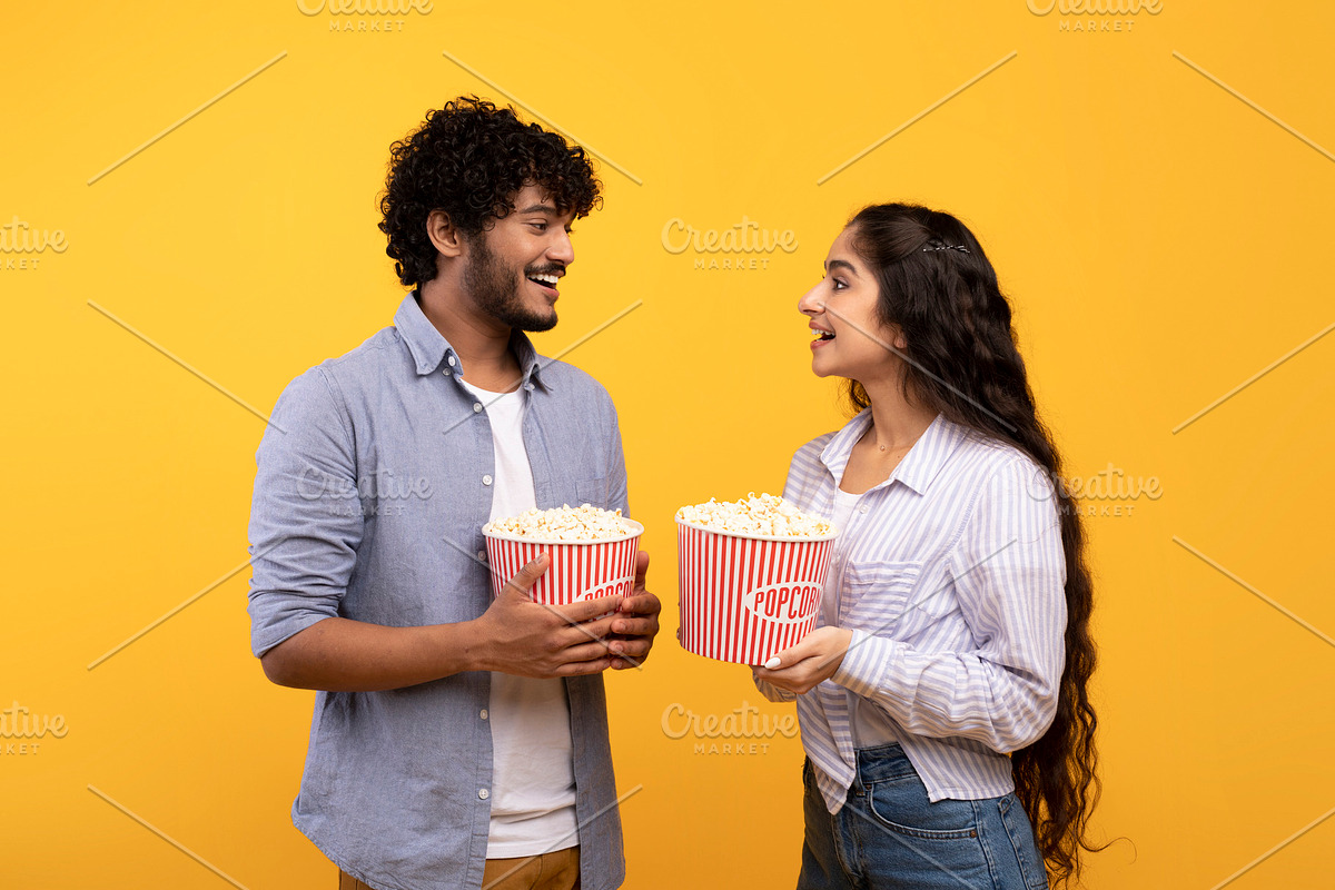Leisure time together. Happy indian man and woman standing with popcorn, lookin, a Photo by Prostock-Studio (Photo 3 of 6)