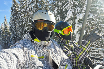Two skiers wearing helmets and goggles on a lift in snowy forest, a Photo by AS photostudio