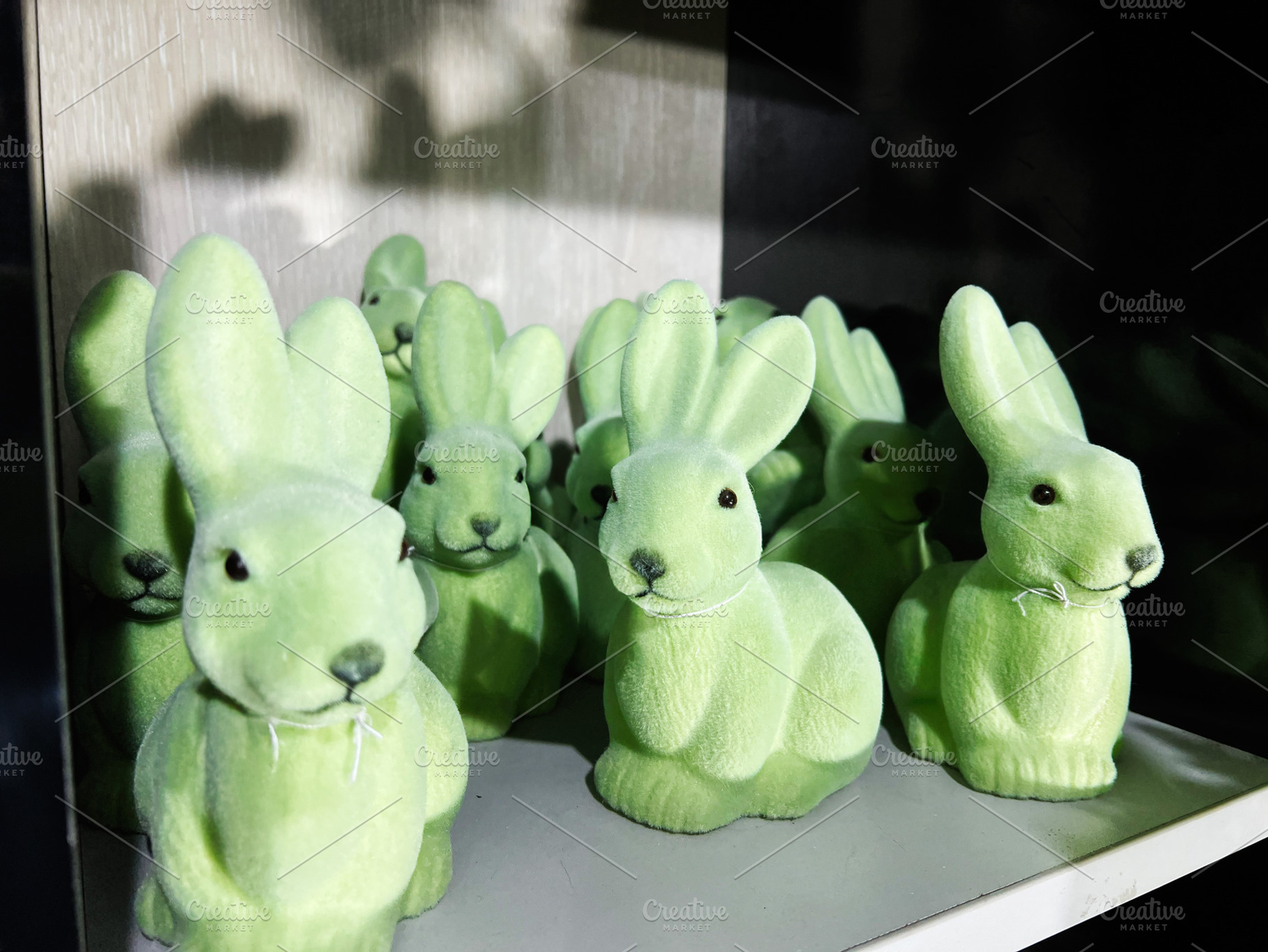 Group of green decorative rabbit figurines displayed on a shelf, a Photo by AS photostudio