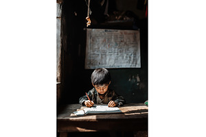 Asian boy concentrating on writing, a Person Photo by Sergey Kotenev