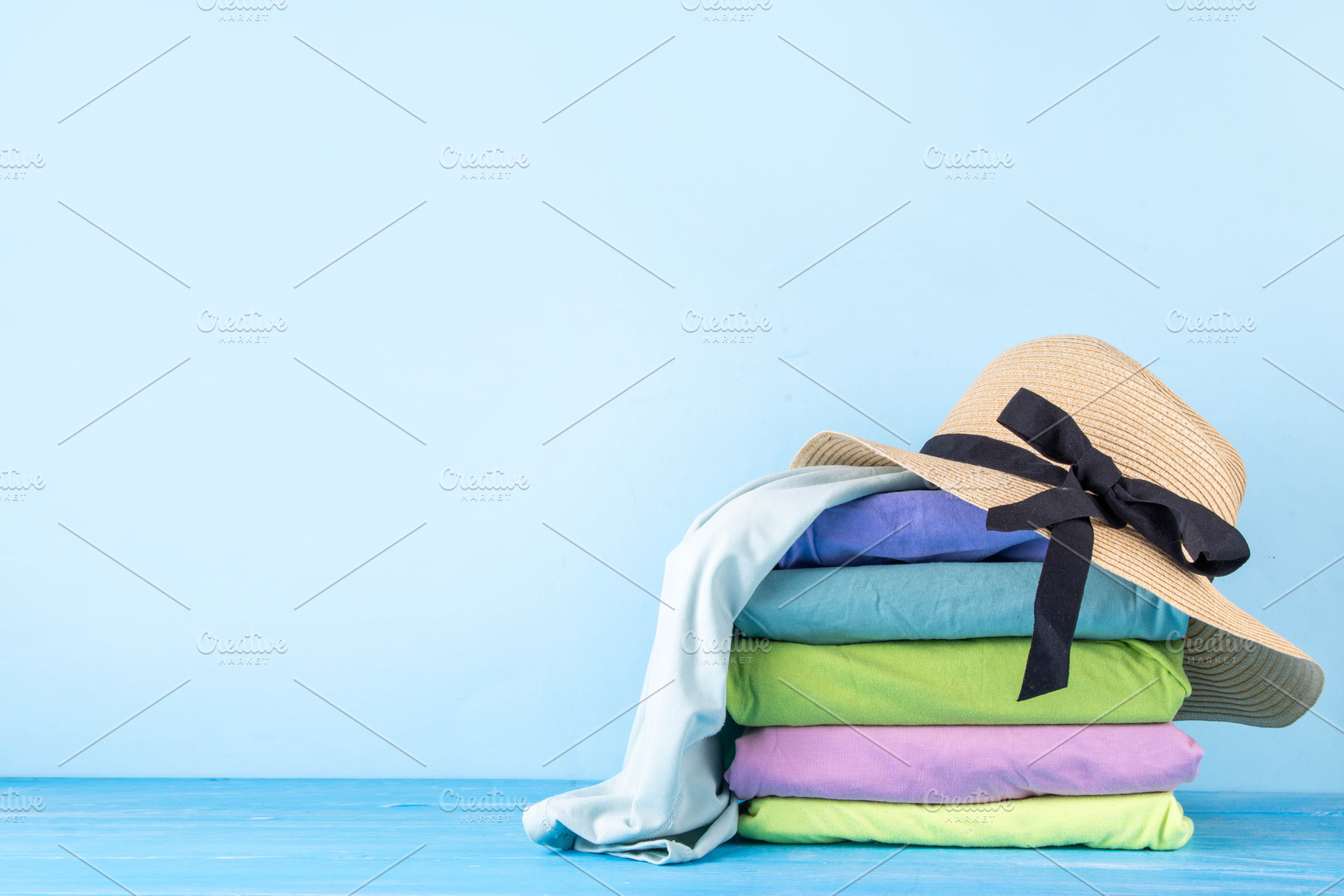 Summer bright clothes pile stack on wooden light blue table, a Holiday Photo by Rimma