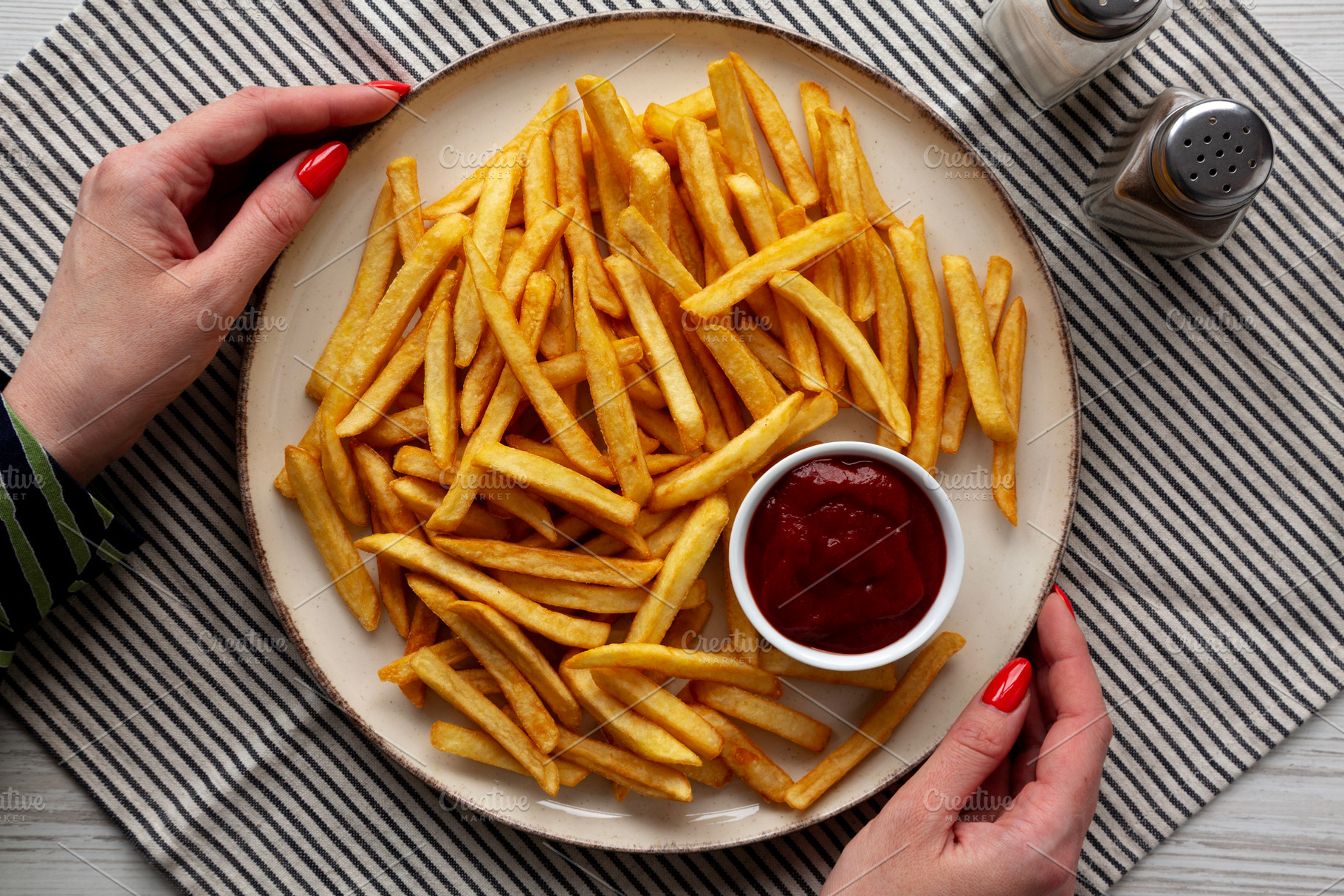 Female hands hold a plate with homemade Golden French Fries with, a Food & Drink Photo by LiudmylaChuhunova