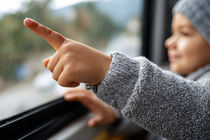 A joyful child points at raindrops on the bus window, wearing a cozy gray sweat, a Business Photo by ImageMir