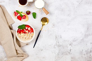 A bowl of oatmeal with strawberries and almond flakes on a table, a Food & Drink Photo by vimart