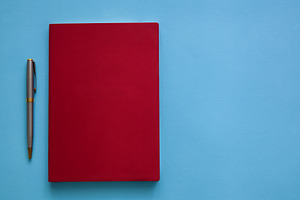 Red notebook with pen on blue background, an Abstract Photo by Photostock