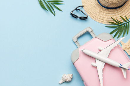 Pink suitcase with toy airplane, sunglasses, straw hat, seashell