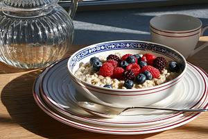 Bowl of warm oatmeal porridge topped with fresh mixed berries on a wooden table, a Photo by Studio ANNA