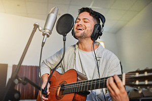 Guitar, microphone and singing in studio for album recording, theatre label or radio musician industry. Man, singer and guitarist headphones for instrument production, theater sound or karaoke media, a Photo by Peopleimages.com