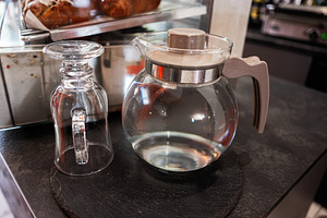 Clear glass pitcher and inverted mug on a dark countertop with pastries nearby, a Photo by AS photostudio