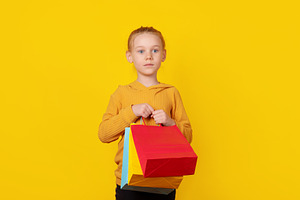 Young girl holding colorful shopping bags against bright yellow, a Person Photo by Ales Munt