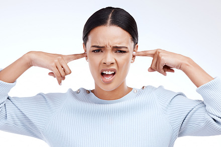 Portrait, woman and finger in ears for noise, silence and denial gesture on studio white background. Omg, face and angry girl with complaint, ignoring and deaf, wtf and emoji, frustrated and annoyed, a Photo by Peopleimages.com