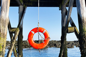 Bright orange lifebuoy hanging under a wooden pier in Portsmouth coastal scene, a Photo by AS photostudio
