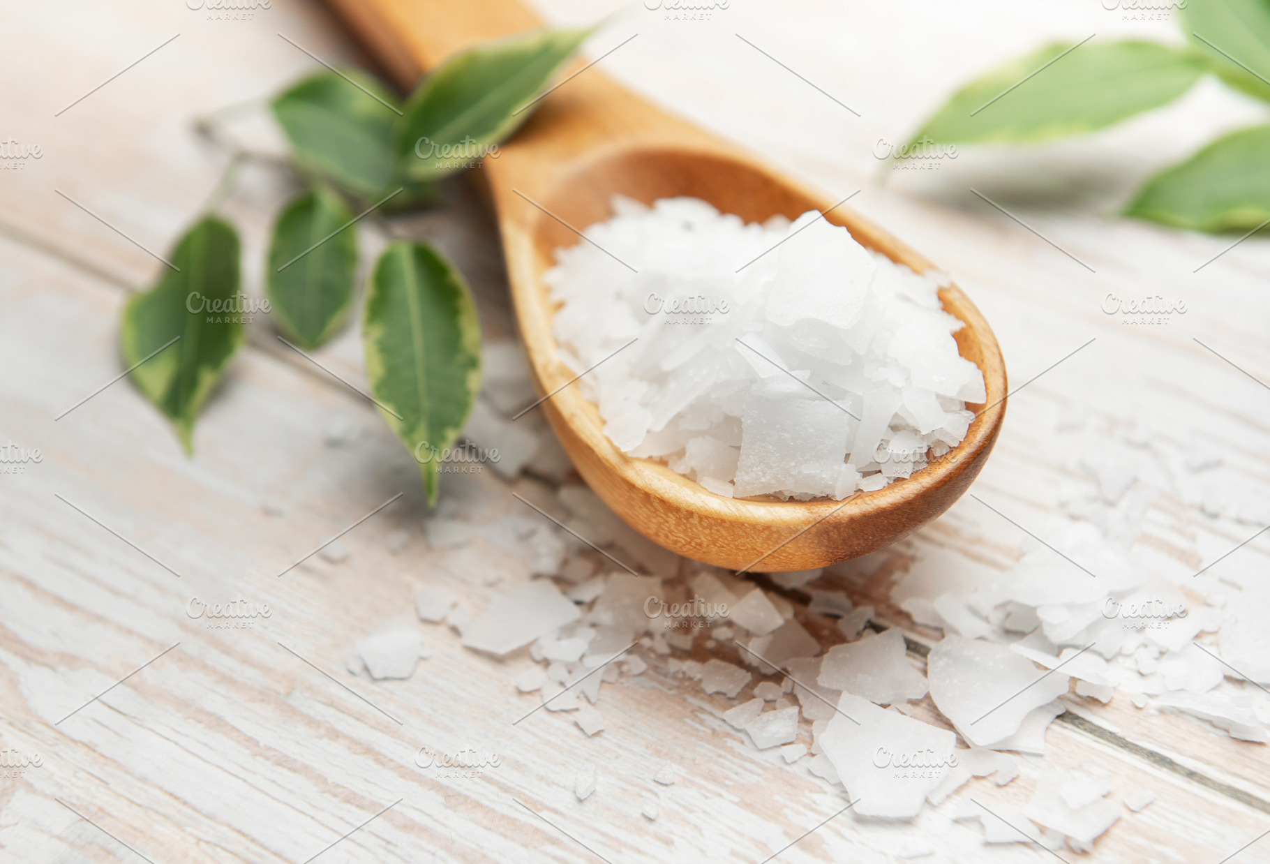 Magnesium chloride flakes on wooden spoon with green leaves, a Beauty & Fashion Photo by Olena Rudo