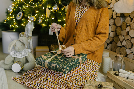 Woman sitting at home under decorated Christmas tree and opening wrapped gift o, a Holiday Photo by Anikona