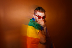 Young adult man wearing red sunglasses wrapped in rainbow flag, a Photo by karrastock