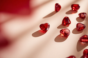 Red crystal hearts scattering on a light background with shadows, a Photo by Studio ANNA