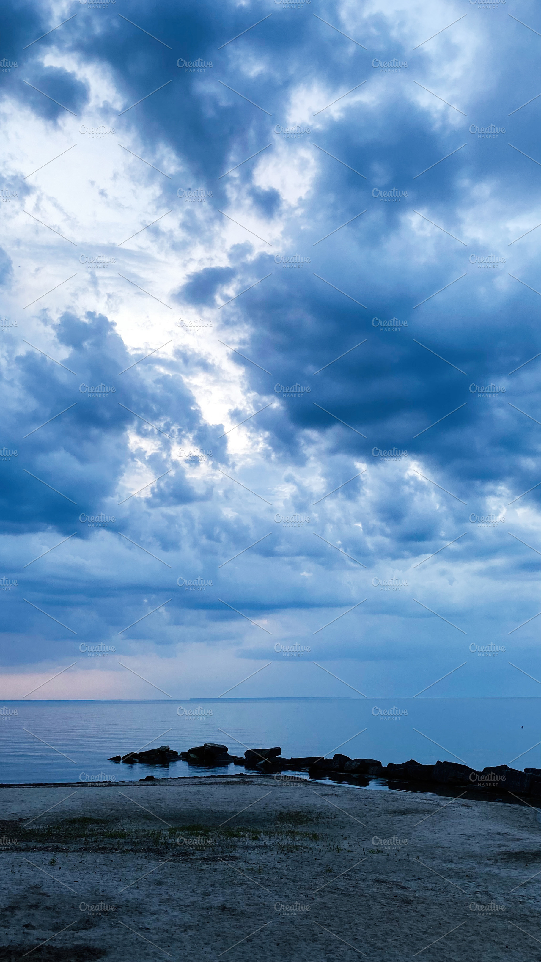 Blue cloudy sky over calm New England shoreline with rocks and quiet sea at dus, a Photo by AS photostudio