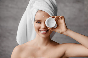 Moisturizing skin after shower. Pretty millennial woman in towel covering her e, a Photo by Prostock-Studio