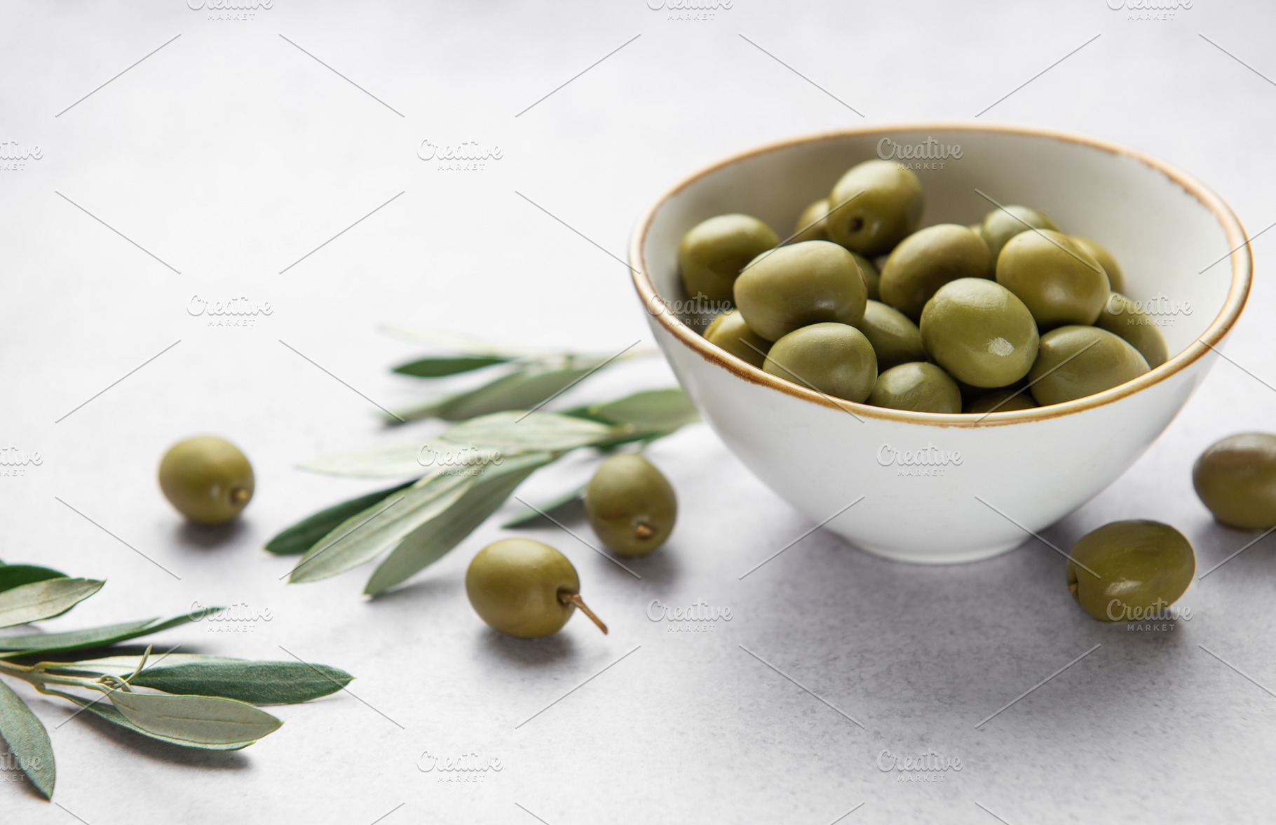 Fresh green olives in a bowl with olive branches on marble table, a Food & Drink Photo by Olena Rudo