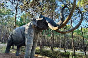 Life size mammoth sculpture amongst trees in a lush forest setting, a Photo by AS photostudio
