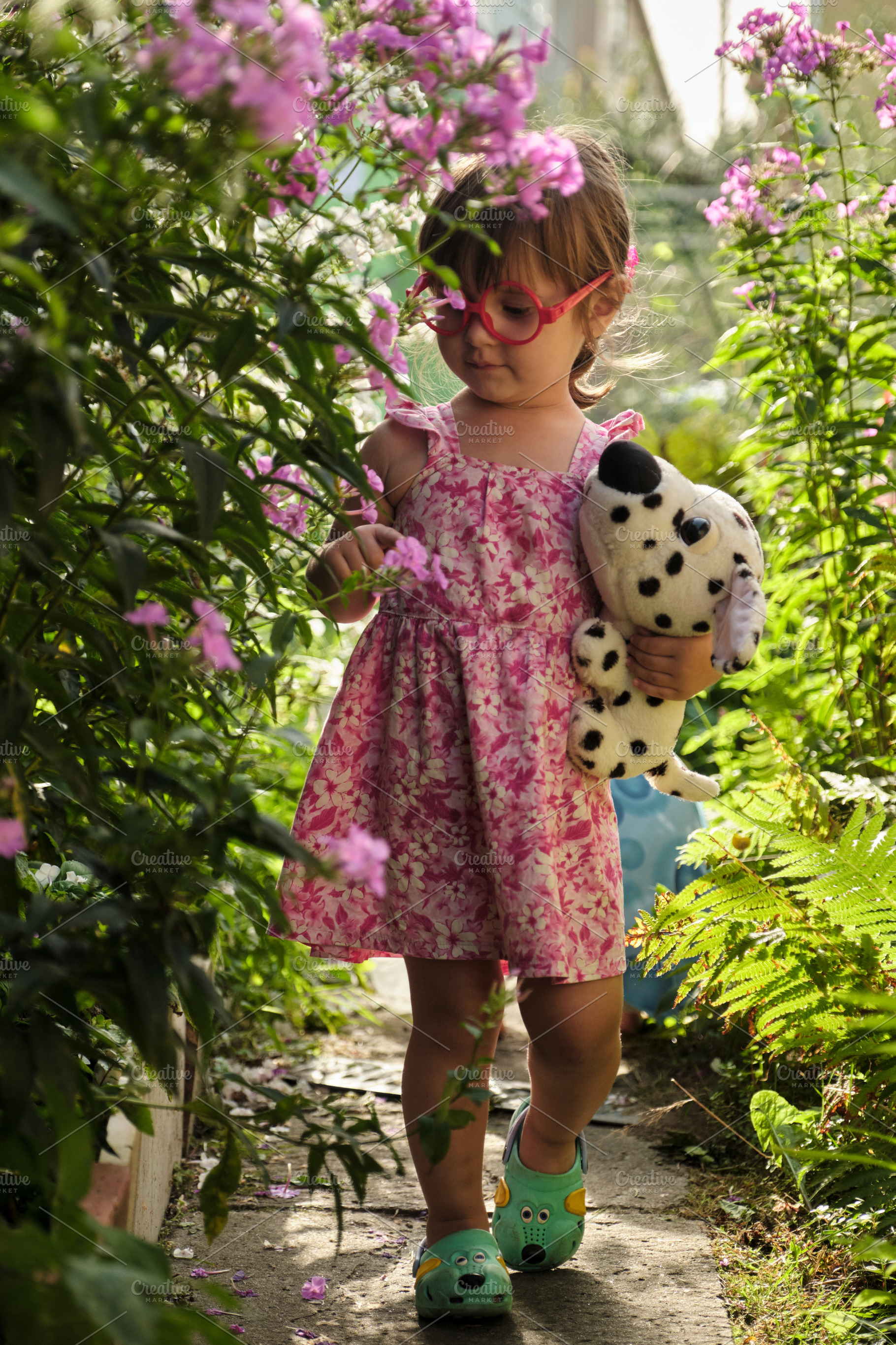 Cute little girl in red toy glasses walking through a blooming summer garden wi, a Photo by Rohan Photography