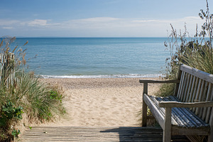 Wooden bench inviting relaxation on a sandy beach leading to the, a Photo by Studio ANNA