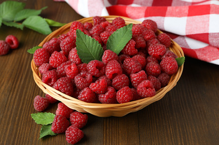 Raspberries in a wicker bowl and a tea towel on a wooden table, a Food & Drink Photo by AtlasStudio